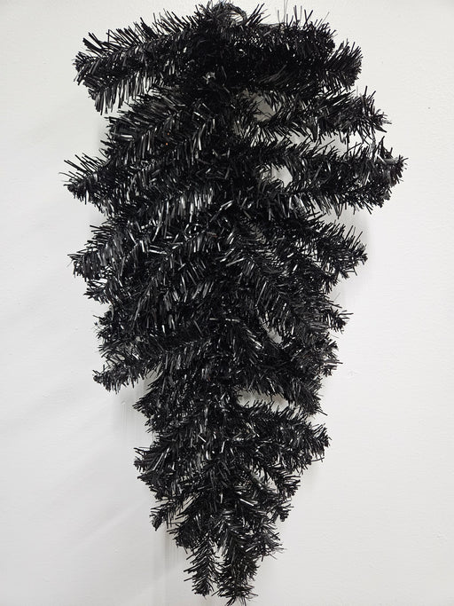 The 24 Halloween Teardrop Black 82298-BK hangs upside down against a white wall, featuring shiny black needle tinsel branches with no decorations.