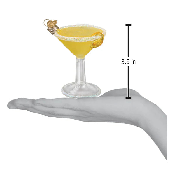 The 3.5-inch Lemon Drop Martini Old World Christmas Ornament 32631 fits in a hand, showcasing yellow liquid with a lemon slice and a charm on the rim—an enchanting decoration.