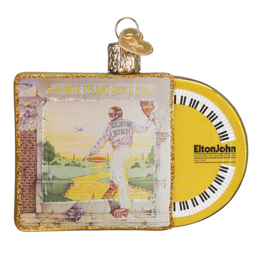 The Goodbye Yellow Brick Road Album Old World Christmas Ornament (38067) exquisitely displays the iconic album cover by Elton John. It includes vivid artwork of a figure stepping onto a yellow brick road, accompanied by a round disc featuring a keyboard design and text. This ornament is an ideal gift for fans of the album.