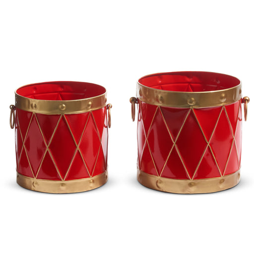 The 10.5" Red and Gold Drum Containers (4425918) are festive, cylindrical metal tins with gold diamond patterns, rims, and handles—resembling toy drums—ideal for Christmas Shoppe décor. Displayed side by side on a white background.
