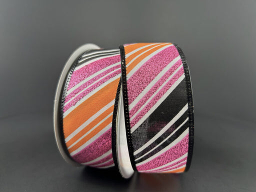 Two spools of 1.5X10Y White Satin/Black-Orange-Fuchsia Glitter Diagonal Stripe Ribbon partially unspool, revealing their vibrant patterns and glittery texture against a dark background.