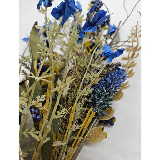 A bouquet with dried plants and vibrant royal blue flowers features a 24 Royal Blue Lavender Berry Spray (63048-RO BL), accented with yellowish-green leaves and twigs, set against a plain, light background.