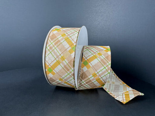 A 1.5X10Y Ivory Moss Mustard Brown Argyle Plaid Ribbon (65525-09-35), featuring a tan, yellow, green, and white plaid pattern, sits on a dark surface with the ribbon partially unrolled and extending outward.
