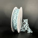 A spool of 7/8X10Y Lt Blue Scallop Weave Burlap Ribbon (67348-05-05) stands upright against a dark background. A loose section elegantly drapes to the side, highlighting its delicate pattern.