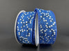 A spool of 1.5X10Y Royal Blue Linen/White Glitter Berries ribbon sits against a dark background, partially unwound to reveal its elegant berry and branch design, adding a touch of sophistication.