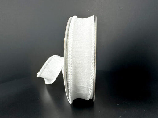 A spool of 7/8X10Y White Faux Dupioni Ribbon (72434-05-01) stands upright on a black background, with some white ribbon unspooled and trailing to the side.