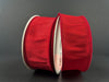 Two rolls of 1.5X10Y Red Faux Dupioni Ribbon 72434-09-12 with a slightly shiny texture stand upright against a dark background, partially unspooled and facing each other.