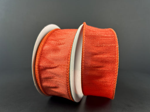 Two large spools of 1.5X10Y Orange Faux Dupioni Ribbon 72434-09-19 are set against a dark background, showcasing their textured appearance and shiny finish, with visible edges that suggest a satin-like or organza material.