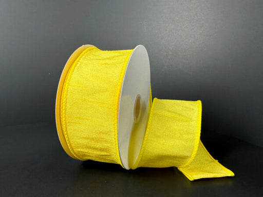 A spool of 1.5X10Y Daffodil Faux Dupioni Ribbon (72434-09-22), in bright yellow with a slightly textured, shiny finish, is partially unrolled on a dark surface against a black background.