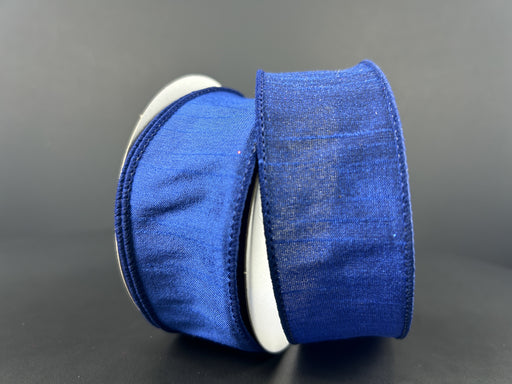 Two rolls of 1.5X10Y Navy Faux Dupioni Ribbon 72434-09-27 stand against a dark background, with one textured spool partially unrolled and draped over the other, both positioned upright to add dimension to the scene.