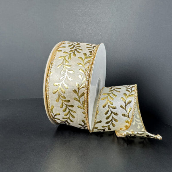 A spool of 1.5X10Y Ivory Satin/Gold Embossed Vines Ribbon (73528-09-41) with a gold leaf pattern and gold edges rests against a dark background, partially unrolled and elegantly draping to the side.
