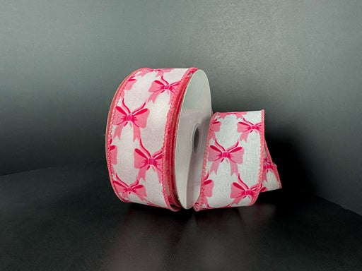 A spool of 1.5X10Y White Ponche Satin/Pink Bows Ribbon 73543-09-03 features pink bows on white satin, with one end unrolled and curved beside the spool, set against a plain dark background.