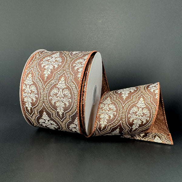 A 2.5x10Y Brown Satin/Demask Quatrefoil Ribbon (73556-40-38) with a white and gold ornate pattern is displayed on a dark surface, partially unrolled and elegantly draped in front.