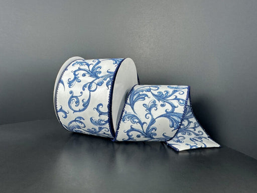 The 2.5X10Y White Glass Satin/Chinoiserie Swirls Ribbon (73567-40-27) features elegant blue ornate florals on white, perfect for adding sophistication to decor. Shown partially unrolled on a dark gray surface and background.