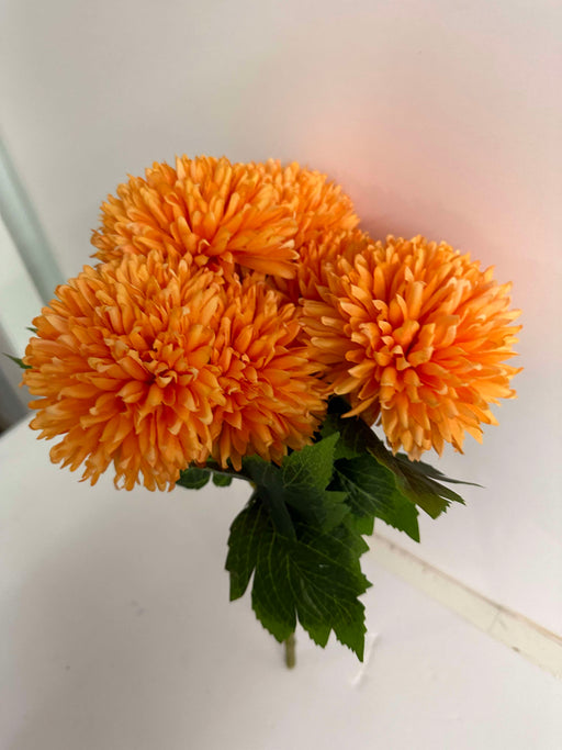 The 16 In Mum Bush X 7 84700-Or, featuring seven vibrant orange chrysanthemum stems and lush green leaves, stands out against a plain white background.