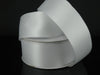 The 1.5 by 25 Yards White Wired Double Faced Satin Ribbon 950109-01 glistens subtly as it unwinds from its coil on a black surface, offering a smooth texture perfect for any sophisticated project or decor.