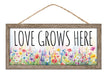 The 12.5L x 6H Love Grows Here sign, AP7386, features a rustic MDF design with rope hanging and vibrant floral illustrations of poppies and daisies, making it a lively addition to any home decor.