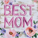 The 10 x 10 Best Mom Sign (2) TTE-222 features pink BEST MOM text centered on white wood, surrounded by watercolor-style pink, purple, and green flowers—ideal for heartfelt home decor.