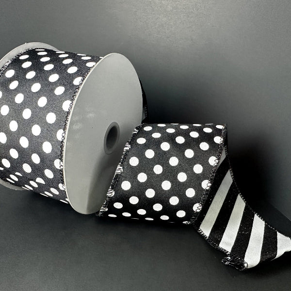 A 2.5 x 10 yd double-sided ribbon spool (D73582-40-20) in black satin with large white dots on one side and black-white glitter candy cane stripes on the other is partially unrolled against a plain black background.