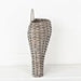 The 11 by 13.5 by 4 Curvy Basket (M21202IEI) features a tall, narrow shape with a rounded base, textured weave, and single curved handle. Its shown against a white wall on a light surface.