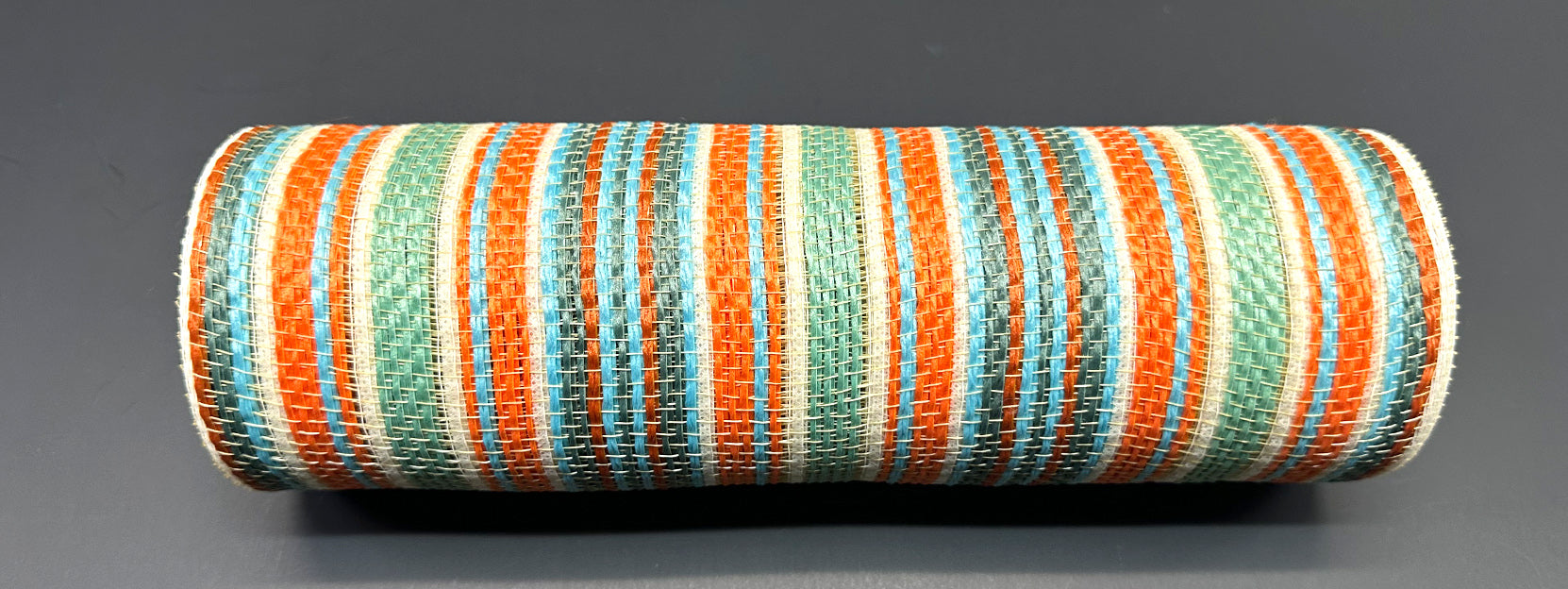 A cylindrical object with a woven look, featuring teal, rust, and ivory stripes like the 10X10Y Rust-Teal-Ivory Striation Mesh XB240910-33, set against a dark gray background.