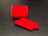 A spool of Bright Red Velvet, 4X10Y Ribbon (131804-13) is partially unrolled on a dark surface, displaying its smooth texture and synthetic wired edges as it curves gently.