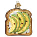 The Avocado Toast Old World Christmas Ornament 32442 is a decorative ornament shaped like avocado toast with cream cheese, featuring a gold hanging loop—a playful tribute to the popular food trend.