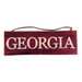 The Red Black Georgia or Go Team Assorted Wall Hanging AP809899 features a rectangular MDF wooden sign with a red background and visible grain patterns, displaying GEORGIA in large white capitals, and is suspended by a brown rope.
