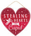 The AP8985 is a 12L x 11.5H heart-shaped Cupid Glitter Sign featuring a Cupid illustration and the phrase Stealing Hearts Like Cupid on a red background with white hearts and dots, complete with an attached rope for easy hanging.