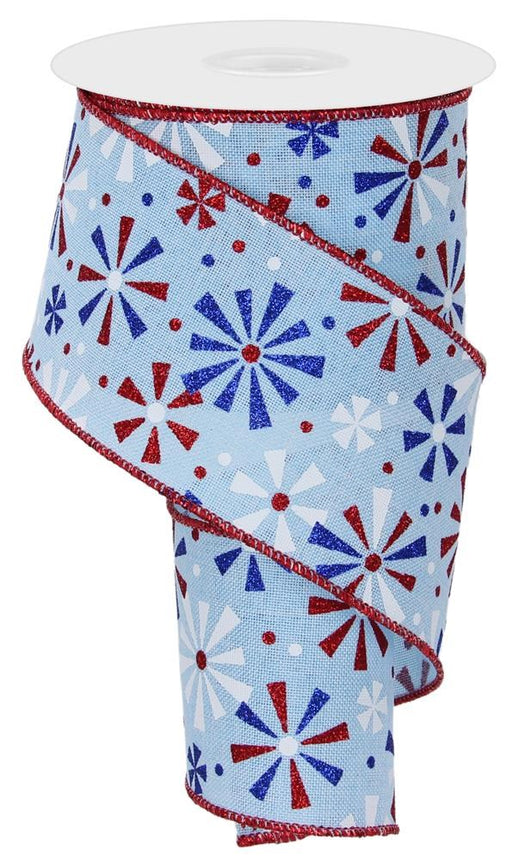 The 2.5X10Yd Pale Blue Red Blue White Vintage Pinwheels Rge115614 ribbon features a light blue background with vintage pinwheel starburst designs in red, white, and royal blue. It is wired and partially unwound, with glittery red edges that enhance its festive charm.