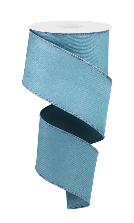 A spool of 2.5X10Yd Diagonal Weave Fabric Smoke Blue RGE1203H5 ribbon with stitched edges unfurls in a spiral pattern on a white backdrop. The wired ribbon is coiled at the top, cascading down gracefully, highlighting its elegant design.