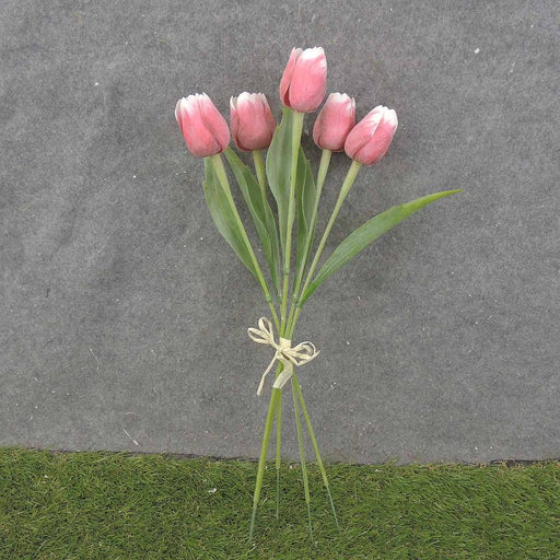 A delightful bunch of 17 red and white tulips with five plastic stems, wrapped delicately with a thin beige string, sits on a gray surface, accented by green grass below.