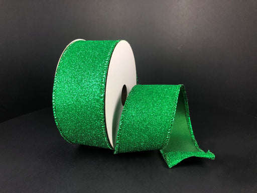 A roll of Emerald All Flat Glitter, 1.5X10Y Ribbon (X820609-17) shimmers in bright green as it’s unspooled against a solid black background—perfect for creative projects.