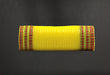 The 10X10Y Yellow Metallic/Spring Plaid Ruffle Edge Mesh (XB107910-49) is a cylindrical object with bright yellow fabric and red and green striped edges, set against a dark background.