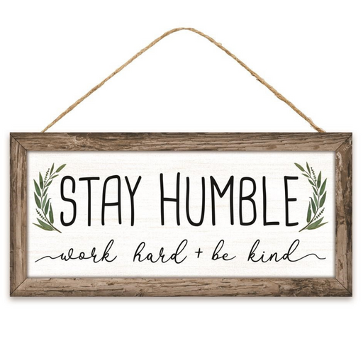 The 12.5 Framed MDF Sign (AP7122) features STAY HUMBLE in large letters, with green leaf illustrations and the cursive work hard + be kind. Its rustic wooden look adds inspirational charm to your home decor.