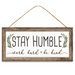 The 12.5 Framed MDF Sign (AP7122) features STAY HUMBLE in large letters, with green leaf illustrations and the cursive work hard + be kind. Its rustic wooden look adds inspirational charm to your home decor.
