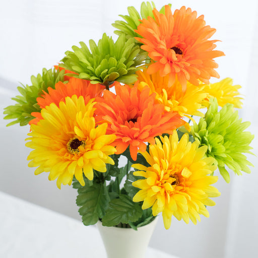 An 18 Citrus Gerber Daisy Bush with 12 stems sits in a white vase, featuring vibrant orange, yellow, and green blooms with lush leaves against a blurred background, creating a cheerful citrus-themed display.