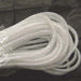 A coiled length of White Silver Foil Deco Flex Mesh Tubular Ribbon RE300440 rests on a dark surface, showcasing its transparent, braided mesh pattern and plastic vinyl-like appearance.