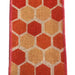 The 2.5 Ivory Canvas Coral Hex Ribbon Q814840-23 showcases a close-up of a rectangular fabric with a honeycomb pattern featuring hexagons in orange and red shades. Red-stitched canvas ribbon edges enhance the design, set against a burlap-like background texture.